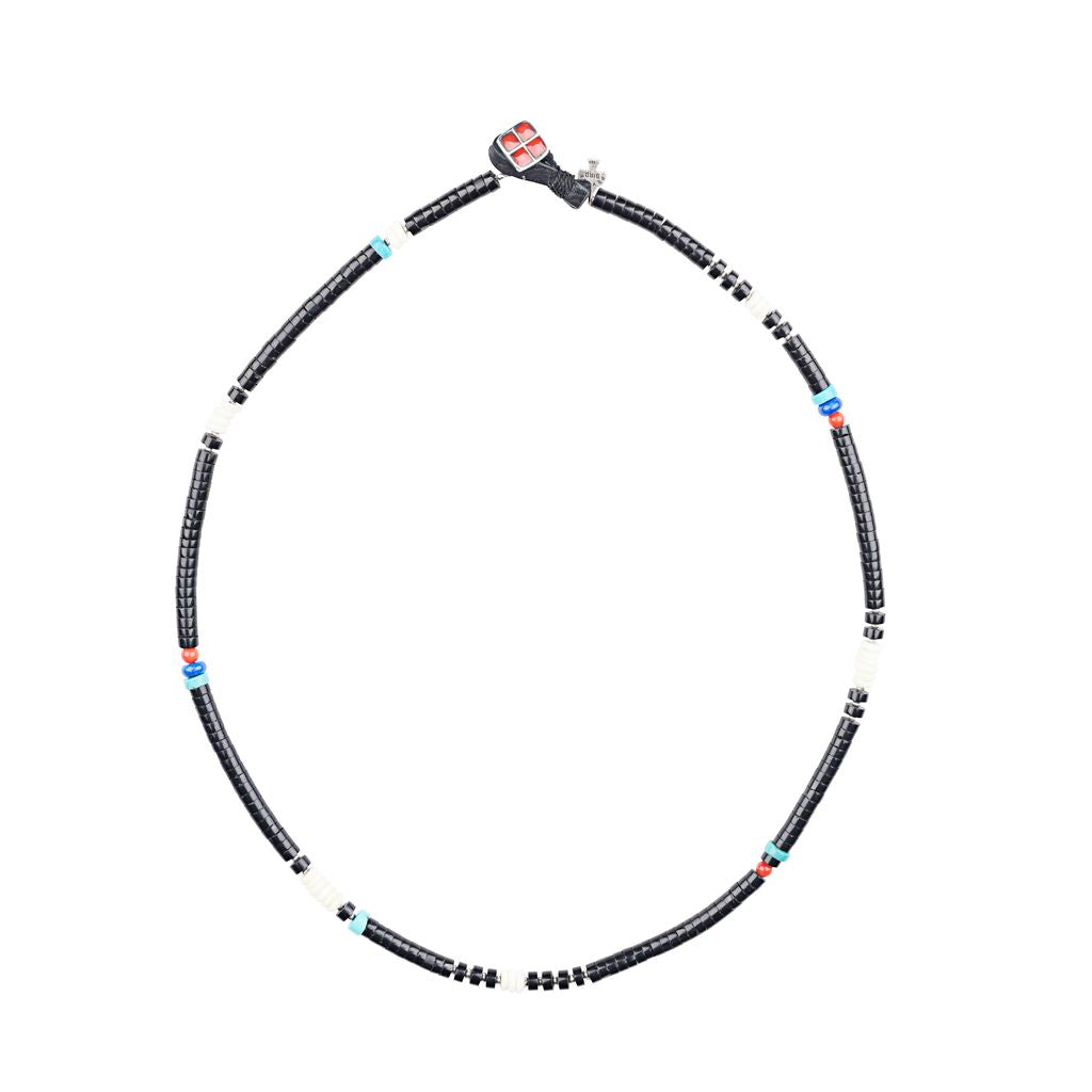 A beaded necklace with black jet heishi beads, featuring pops of color from turquoise, coral, lapis, and bone beads, and a sterling silver and coral button with a deerskin leather loop closure.