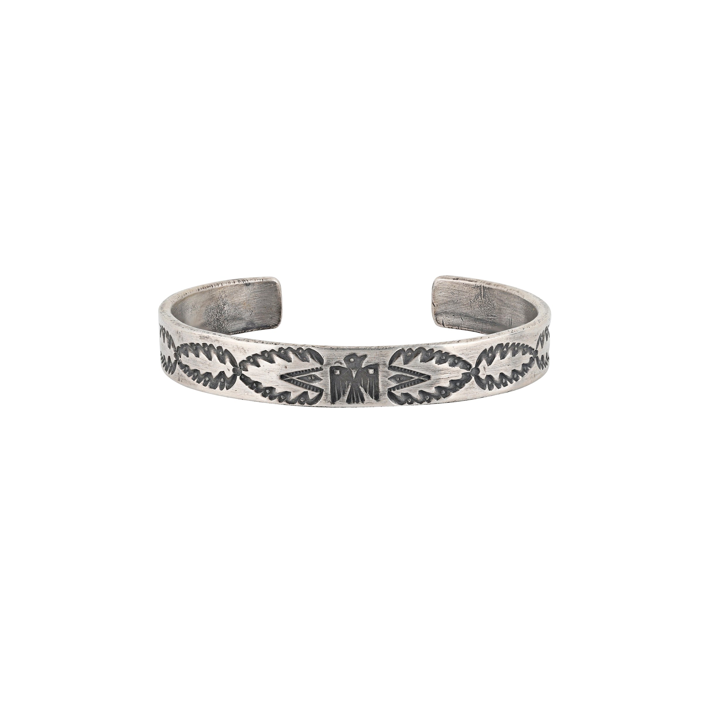 A handmade cuff using Ingot Silver Coin stamped with a Thunderbird as the centerpiece of the cuff surrounded by Southwestern and Santa Fe Style motifs, resembling arrowheads