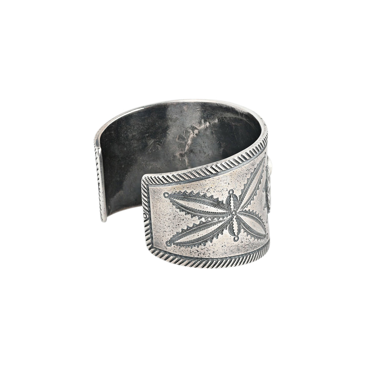 A handcrafted cuff made with ingot coin silver and features a small blue turquoise stone as the centerpiece surrounded by southwestern style motifs