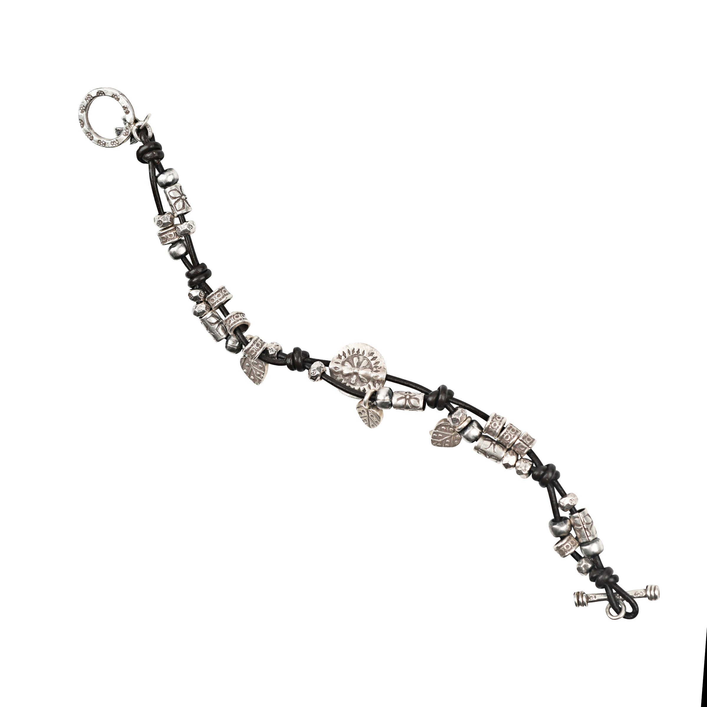 A knotted leather bracelet featuring Sterling Silver charms and beading of leaves, floral accents and stamped Sterling Silver.