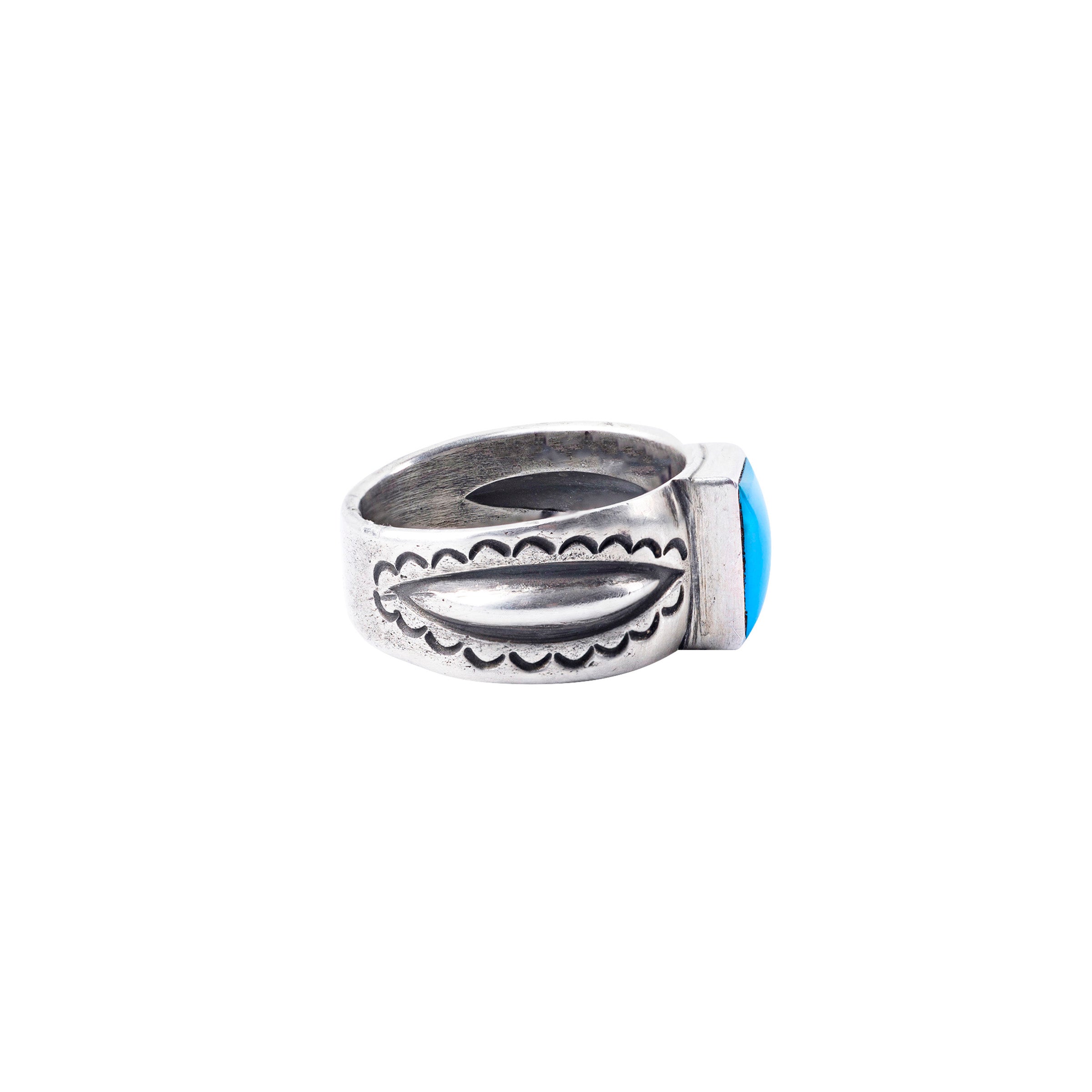 An ingot coin silver ring with a rectangular sleeping beauty turquoise stone inset and intricate designs around the band.