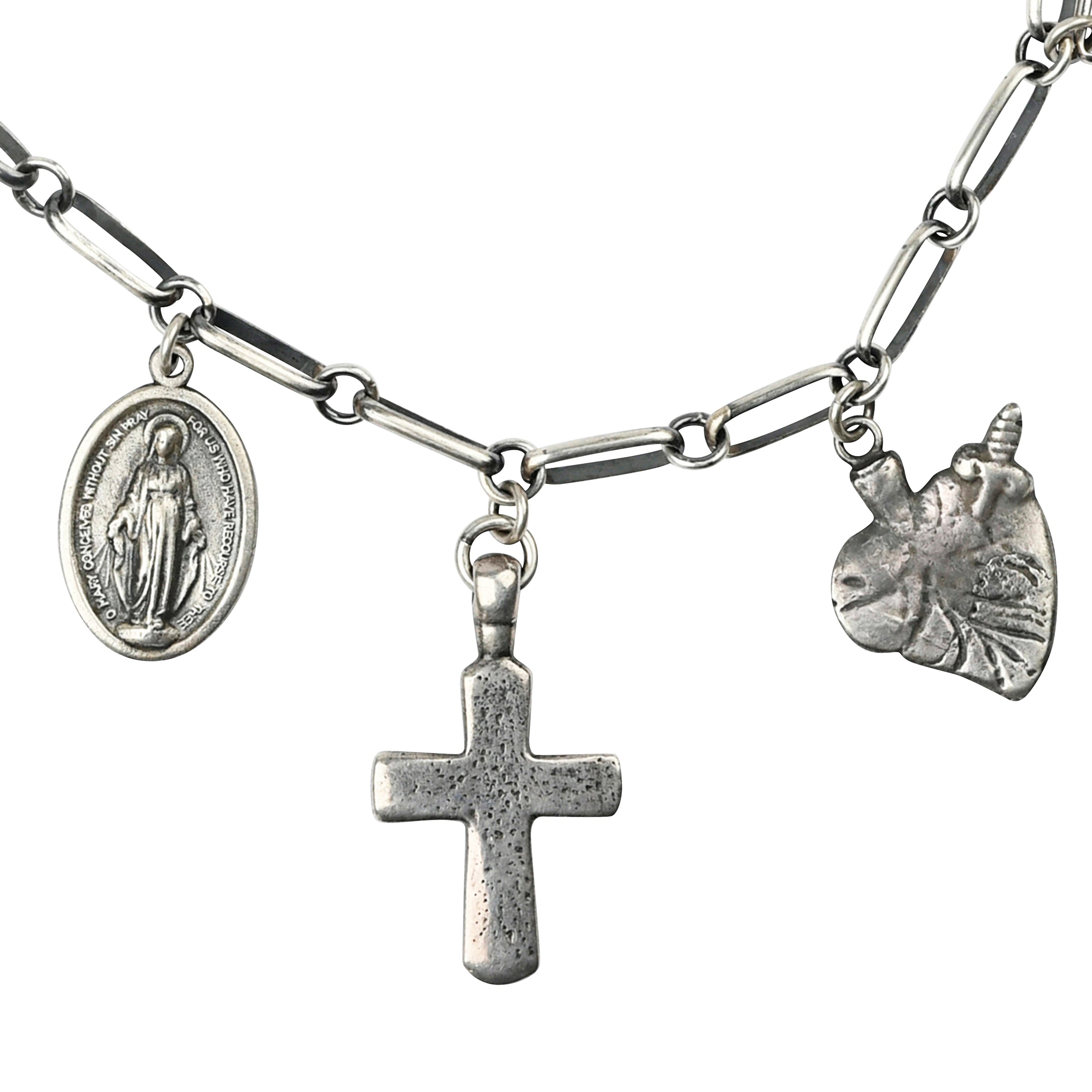 A silver chain necklace featuring the Mountain Spirit Cross Pendant with faith based charms including a Sacred Heart, Mother Mary, a bell, and a Bear totem