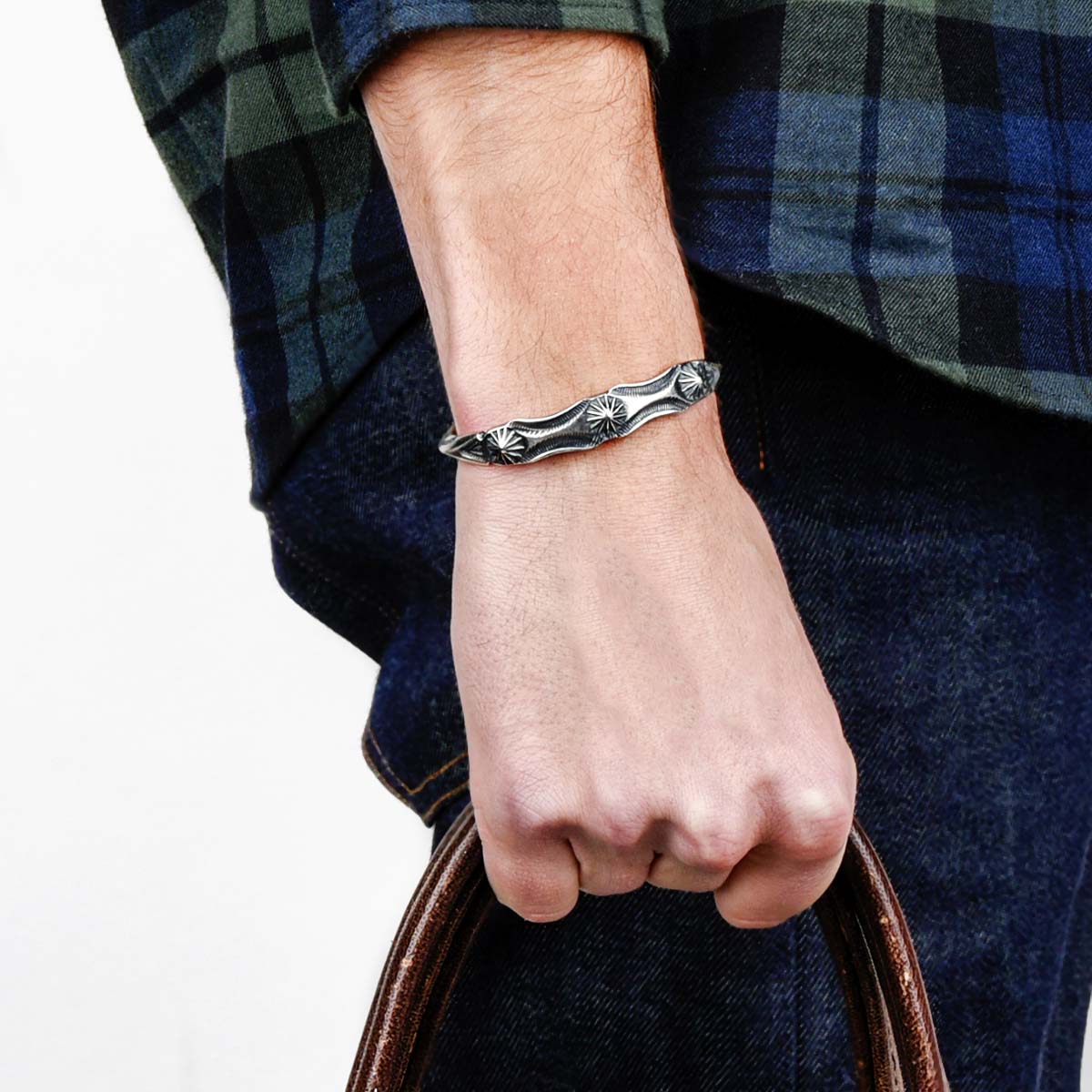 A sterling silver cuff bracelet from artisan Buffalo with intricate stamped geometric patterns and a branded clasp. Made in USA.
