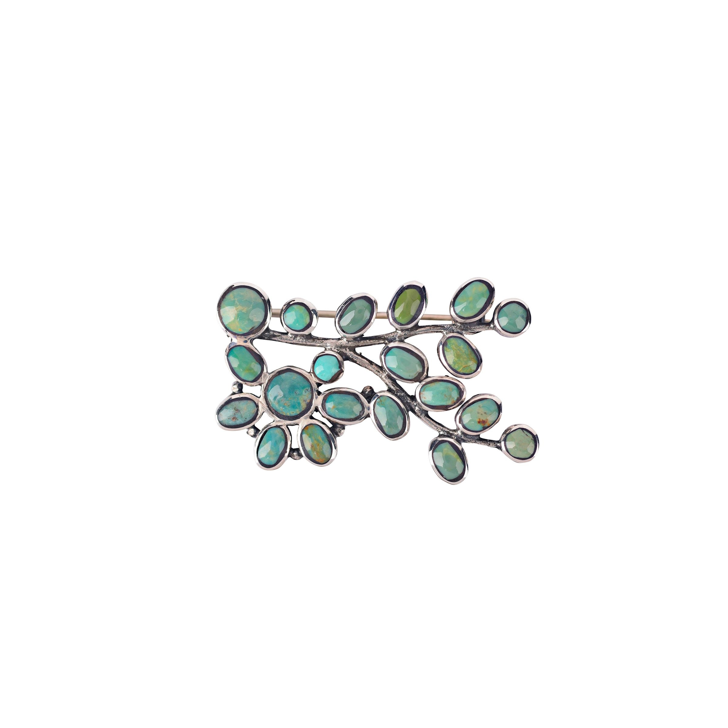 A sterling silver pin with green turquoise stone inlay in the design of a small vine.