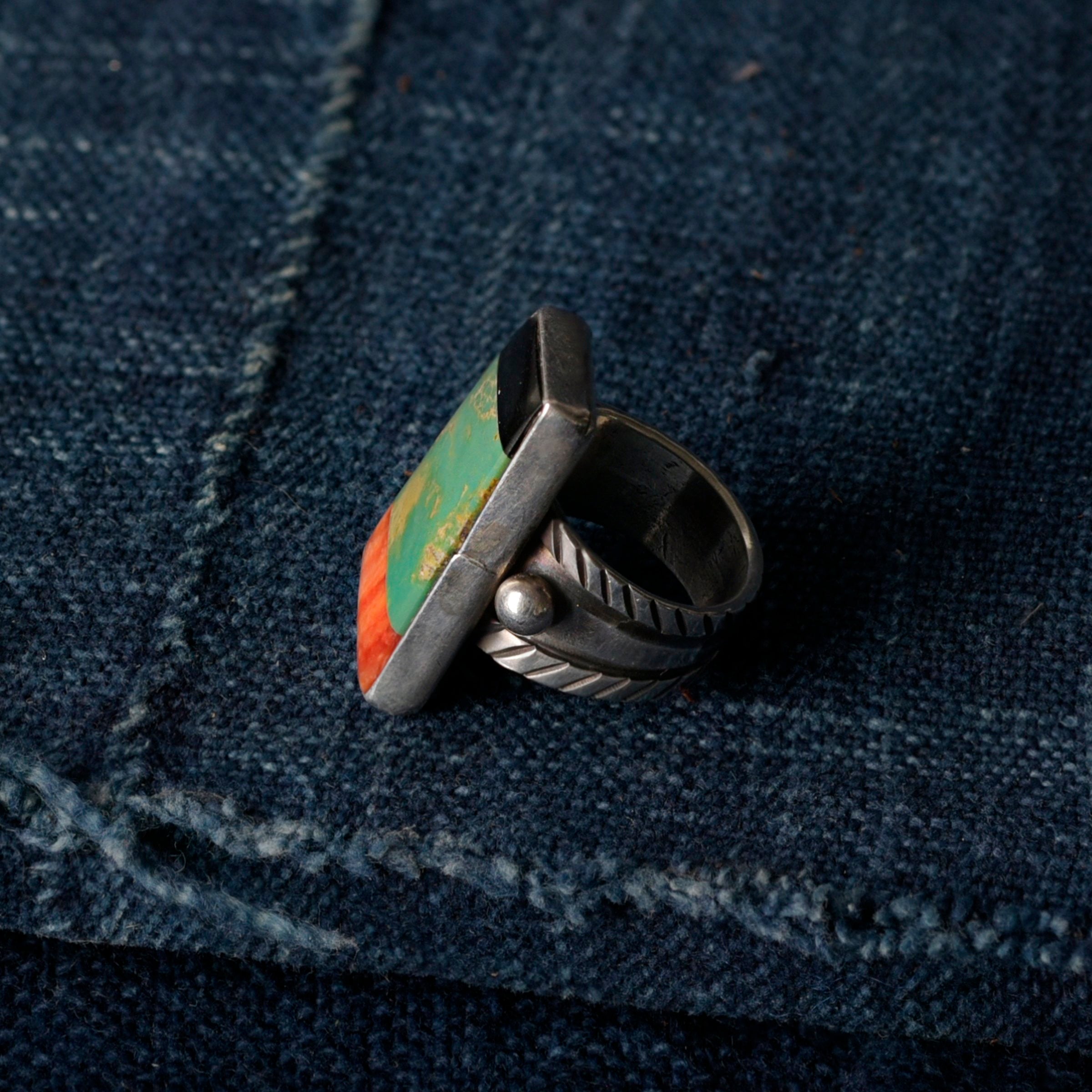 The Forest Floor Ring from artist Jessie Robbins features stamped ingot coin silver with green turquoise, orange spiny oyster shell, and onyx stone inlay. Made in USA.